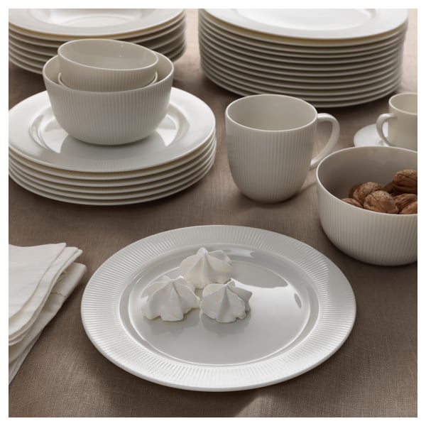 White porcelain dinnerware set with stacked plates, bowls, cups, and meringue. Beige tablecloth and napkin.
