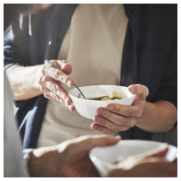 Person holding white bowl with soup, using spoon. Hands visible, wearing black apron.