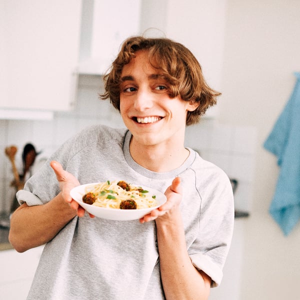 A person holding a bowl of spaghetti and meatballs in a stylish, microwave-safe tempered glass dish.