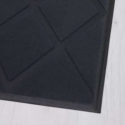 Black door mat with textured polyester surface on light wooden floor.