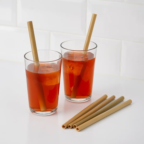 Two tall glasses with dark iced tea and four long bamboo straws, two in glasses, two extra, on white surface.