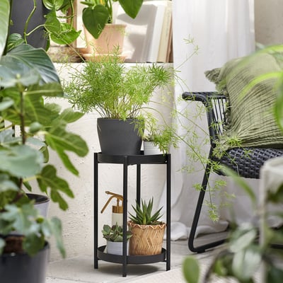 Black OLIVBLAD plant stand with multiple potted plants of varying sizes and shapes. Metal frame, indoor/outdoor use.