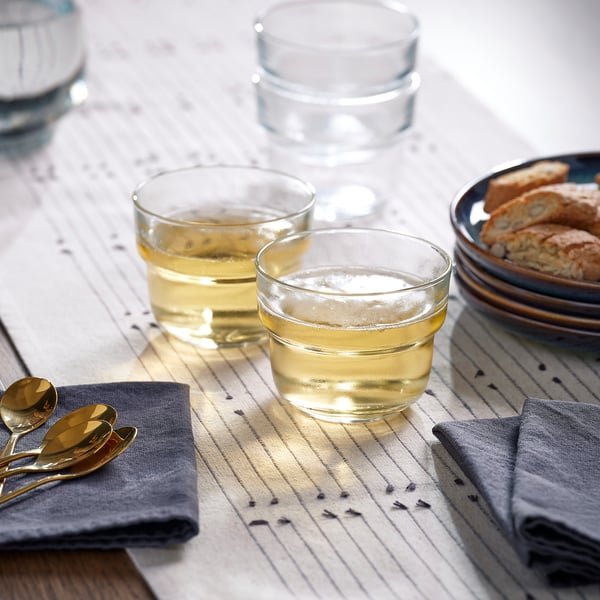 Three glasses filled with liquid on a striped cloth, accompanied by a plate of bread and two spoons.
