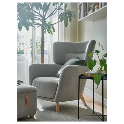Cozy OSKARSHAMN gray chair near large window. Large, cushioned, high-back design. Smaller than the tall plant beside it.