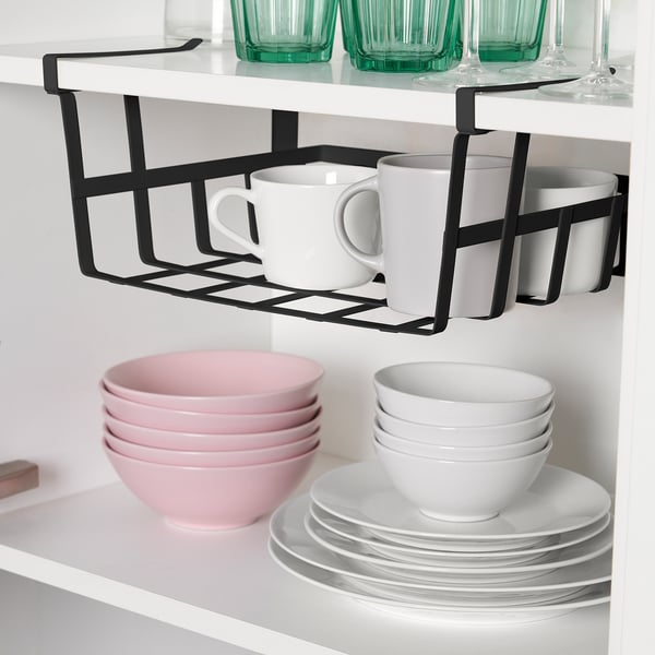Kitchen shelf with PÅLYCKE basket holding mugs, beige bowls, and white plates. Basket clips to shelf for extra storage.