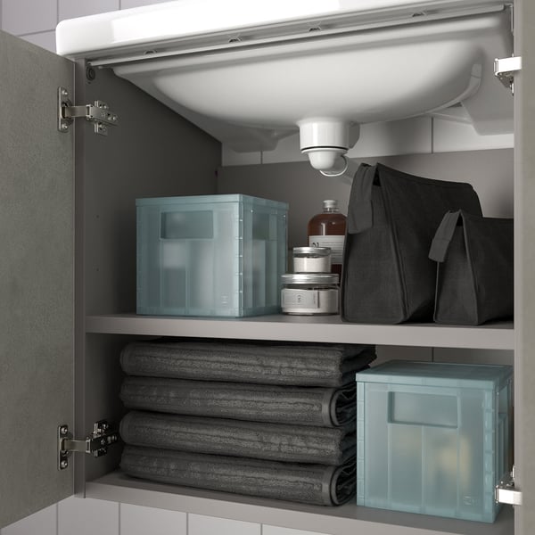 Under-sink cabinet with two shelves, neatly organised bathroom items including stacked towels and blue storage boxes for toiletries.