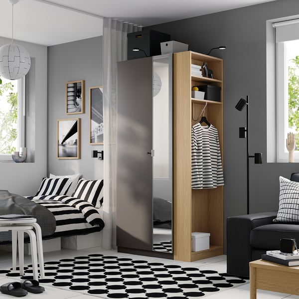 Modern bedroom with PAX wardrobe, black & beige decor. Striped bedding, geometric rug, black sofa, pendant light.