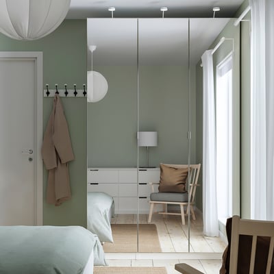 Minimalist bedroom with PAX wardrobe, light green & white. Mirrored doors enhance space. Bed, chair & pillow under window.