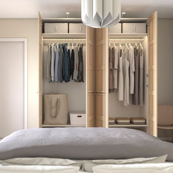 Modern bedroom with PAX wardrobe displaying clothes and storage, featuring adjustable shelves, hanging rod, and closed storage boxes.