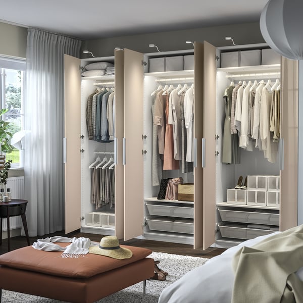 Modern bedroom with open beige PAX closets, showcasing hangers, shelves, and organised clothing. Hinges with dampers for soft door closure.