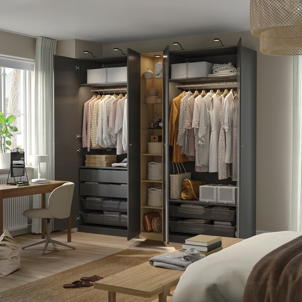 Modern bedroom two open PAX wardrobes showcasing organised clothes, drawers, and shelves. Integrated lighting highlights neatly arranged items.