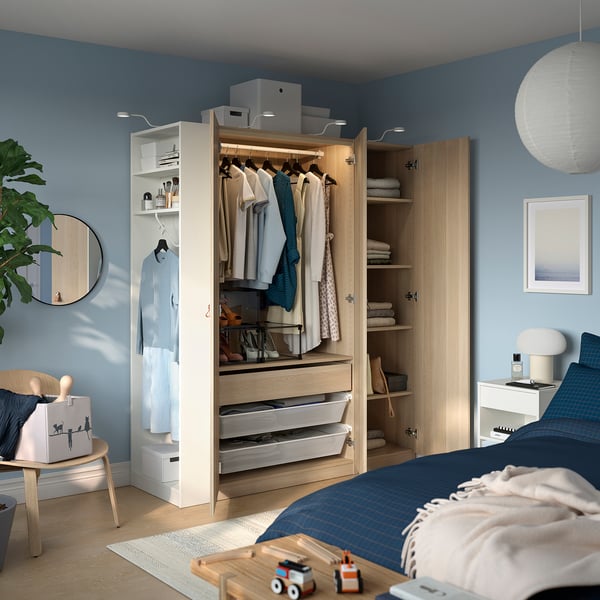 Cosy bedroom with blue walls, a modern PAX wardrobe with clothes, and a bed with toys and a plant.