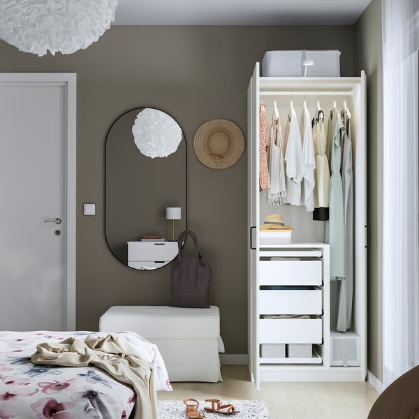 Modern bedroom with open white wardrobe displaying clothes, drawers, and accessories; a round mirror and unique lighting.