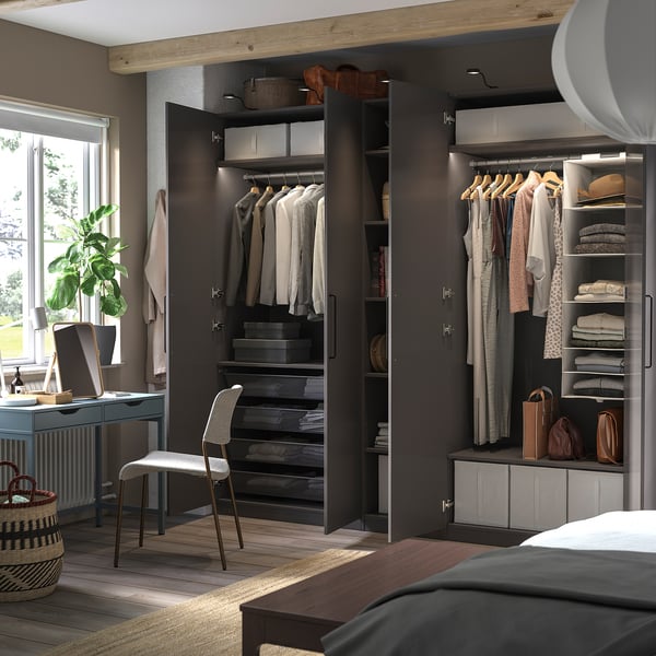 Modern bedroom with open black PAX wardrobe, displaying clothes and accessories, alongside a desk with a chair and a window with a plant.