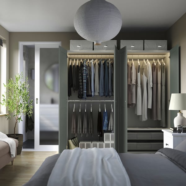 Modern bedroom with open PAX wardrobe, showcasing storage and shelves. Calming grey-green door.