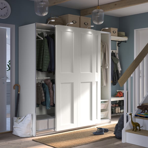 This image shows a white PAX wardrobe with sliding doors, grey rug, and various items like coats and toys around.