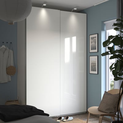 Modern bedroom with white PAX wardrobe, blue walls, wooden chair, plant, and minimalist decor.