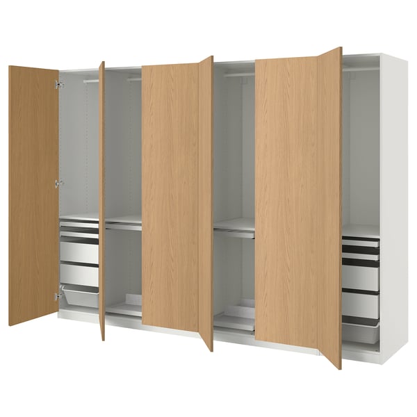 A light wood-colored PAX wardrobe with shelves and drawers. It has three sections, two with open doors revealing storage solutions.
