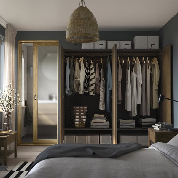 Well-organized bedroom with open wardrobe displaying clothes, folded towels, and storage boxes. A basket hangs from the ceiling.