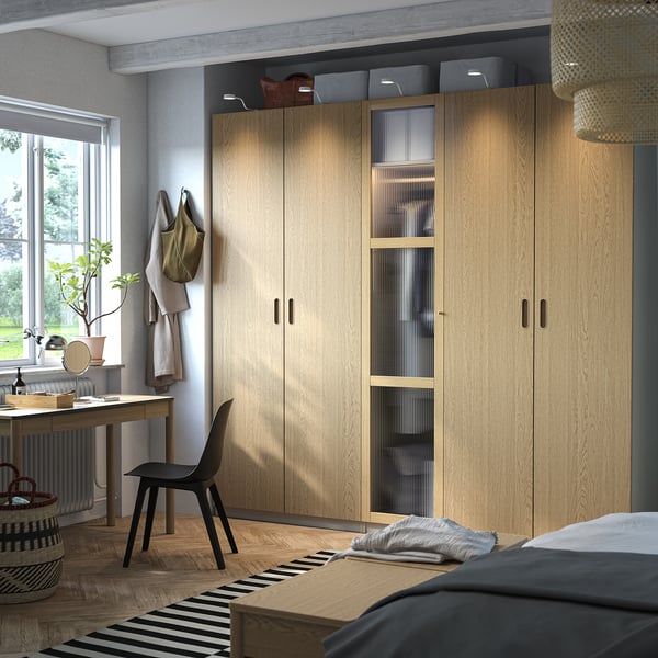 Modern bedroom with large light wood PAX wardrobe, black desk and chair; clean, minimalist design.