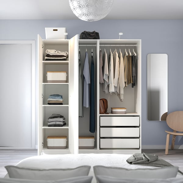 A neatly organised bedroom with an open white wardrobe displaying clothes, folded items, and storage boxes inside.