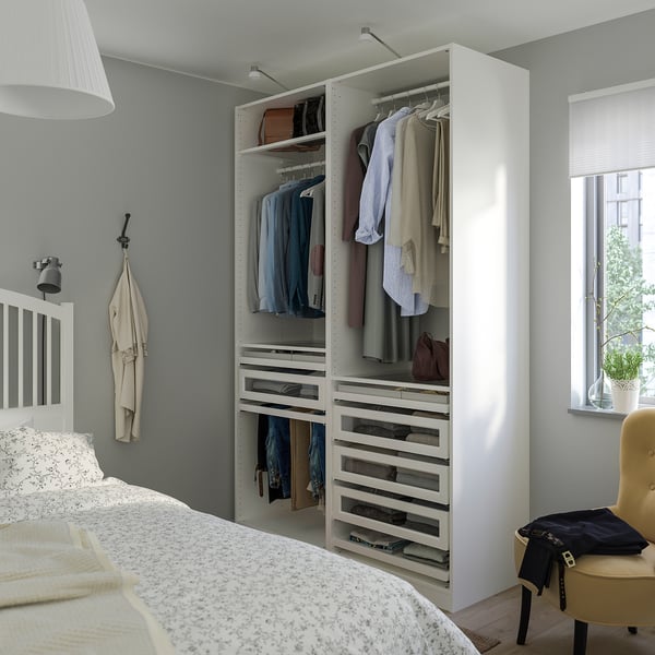 Bedroom with open white PAX wardrobe showing clothing and storage. Wardrobe is tall, wider than bed, with hangers and drawers.
