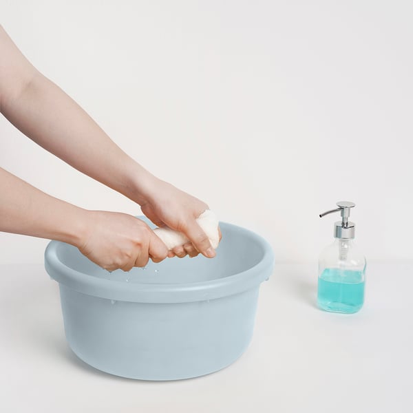 Person washing hands in light blue PEPPRIG bucket next to soap dispenser.