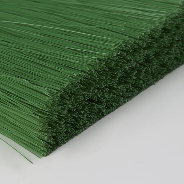 Close-up of a green broom with straight bristles, lying on a white surface.