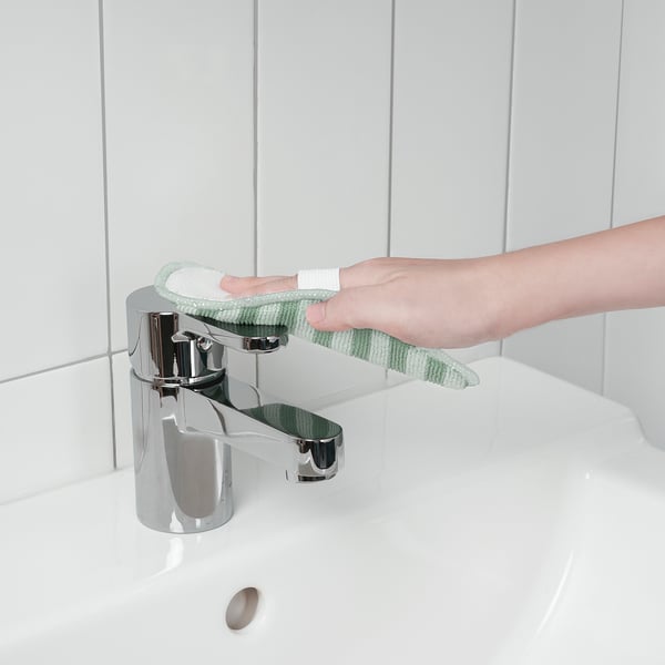 Person cleans sink tap using green microfiber cloth, ensuring glossy surfaces remain undamaged.