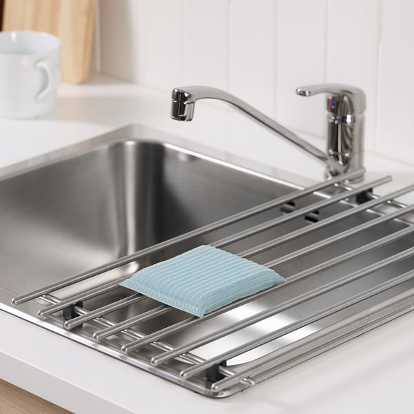 Metal sink with drainer tray holding light green scrubbing pad, chrome tap.