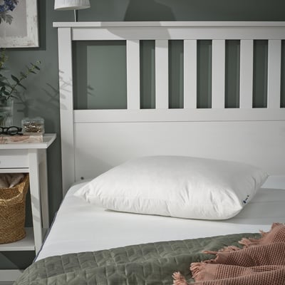 Cosy bedroom with white PILSPINNARE pillow on bed, wicker basket, green quilt, white headboard.