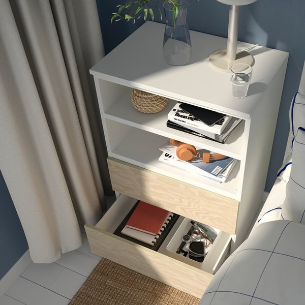 A white PLATSA storage unit with open drawer, near window, holding books and a vase.