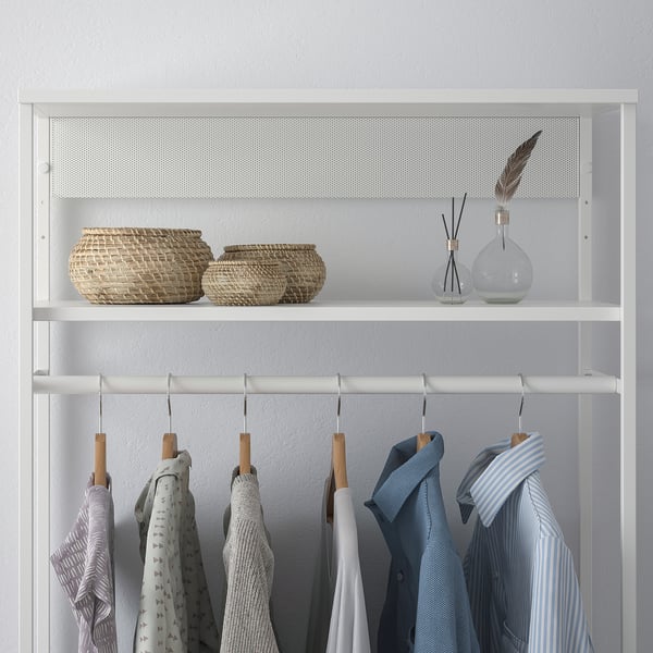 A white closet shelf with baskets, vases, and hanging shirts.