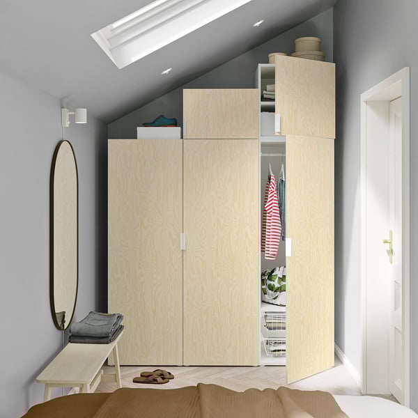 Modern bedroom with light wood PLATSA wardrobe, mirror, bench, and bed. Wardrobe fits under sloping ceiling, larger than mirror and bench.