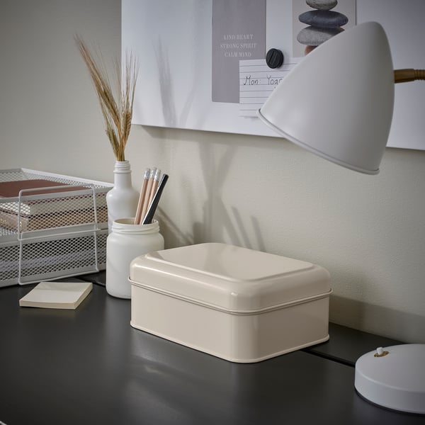 Small white PLOGFÅRA box on a desk, next to a lamp and pens. Organiser fits well with other desk items.