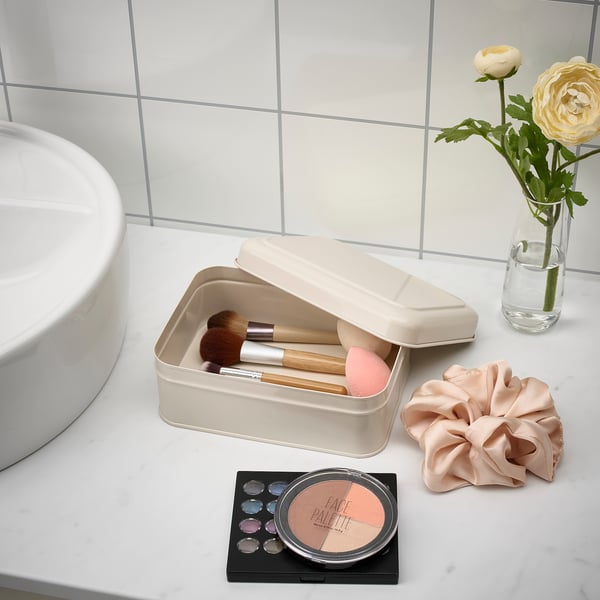 Metal box stores makeup brushes and sponges, sits on bathroom counter, organised, clean look.