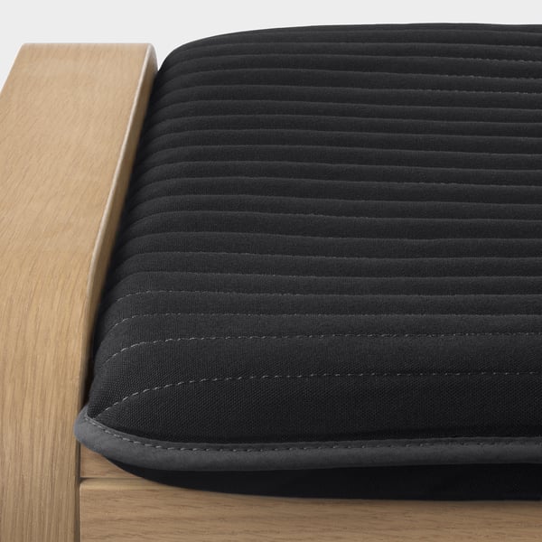 Close-up of a stylish, dark grey cushion with intricate stitching on a wooden surface.