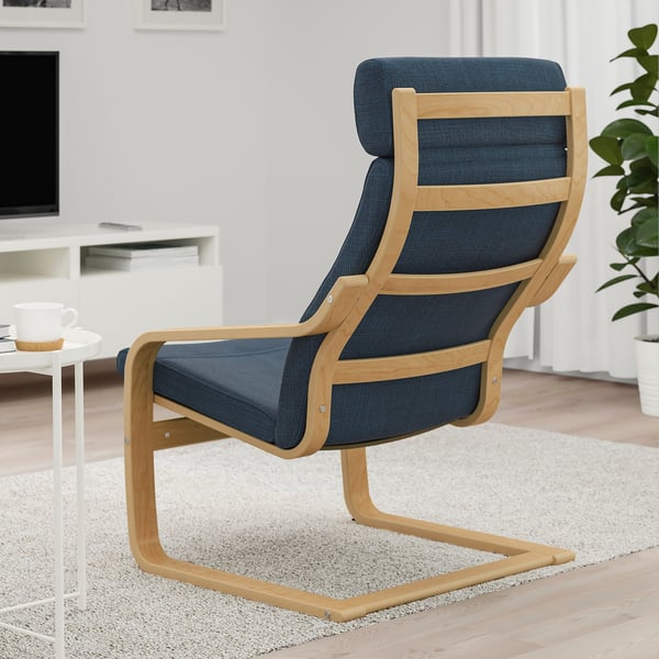 Blue cushioned armchair with wooden frame on living room rug beside white side table with tea cup.