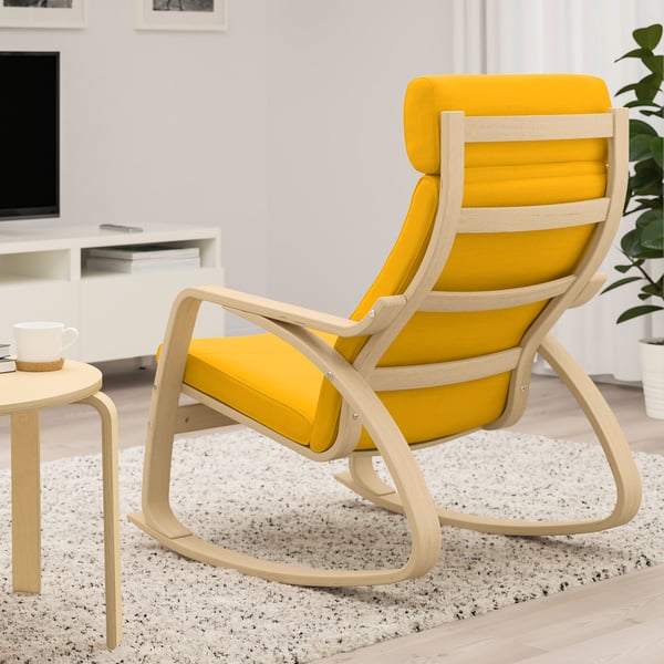 Bright yellow cushioned rocking chair with light wood frame in minimalist living room with white rug and small wooden table.