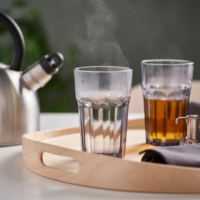 Two tempered glass cups on a wooden tray, one steaming, one with tea, beside a kettle.