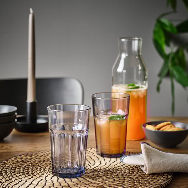 Table set with clear glasses, a pitcher of orange liquid, snacks, and a lit candle.