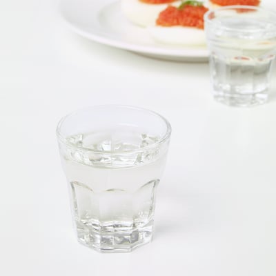 Two glasses with ice sit on a white table, beside a plate with food.