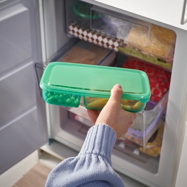 Hand holding green container with food, placing into fridge.