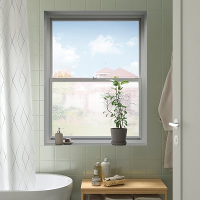 Small bathroom with green tiles, frosted window, and plant.