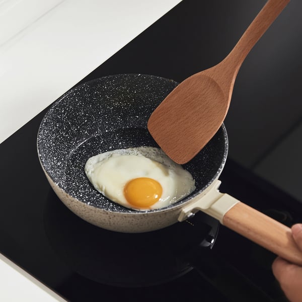 Stirring fried egg with wooden spatula in non-stick pan.