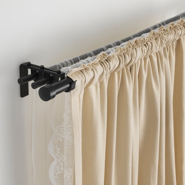 Image shows a black adjustable curtain rod with beige curtains, demonstrating its flexible length and sturdy hold.