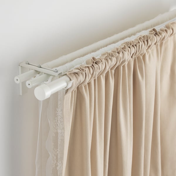 White adjustable curtain rod with beige curtains, mounted on wall.
