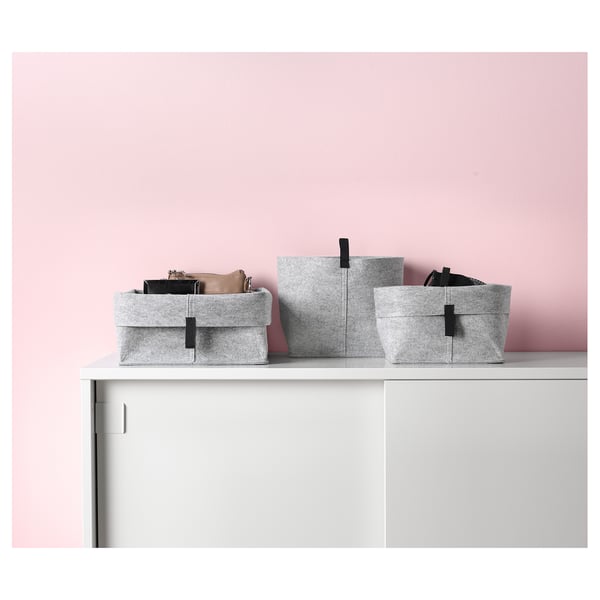Three light grey felt storage baskets on white shelf against pink wall, varied sizes, folded edges.