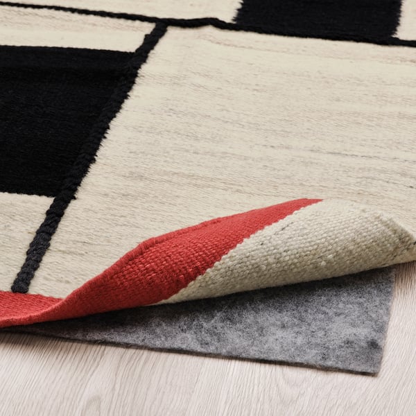 Modern flatwoven rug with geometric design, red edges, and non-slip pad.
