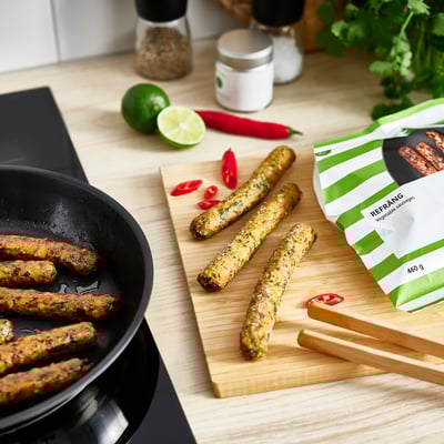Wooden board with cooked vegetable sausages, pan, lime, chilli, packaging labelled refrång.